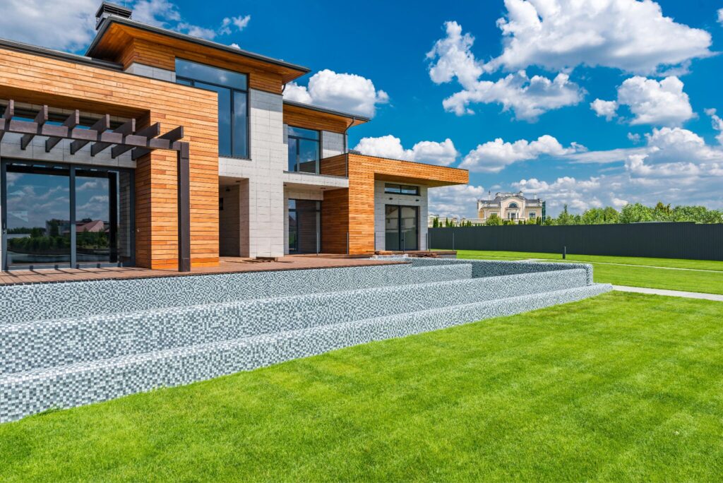 Sandra Rathe Mastering Luxury modern luxury home exterior with large glass windows, landscaped lawn, and contemporary architecture under blue sky