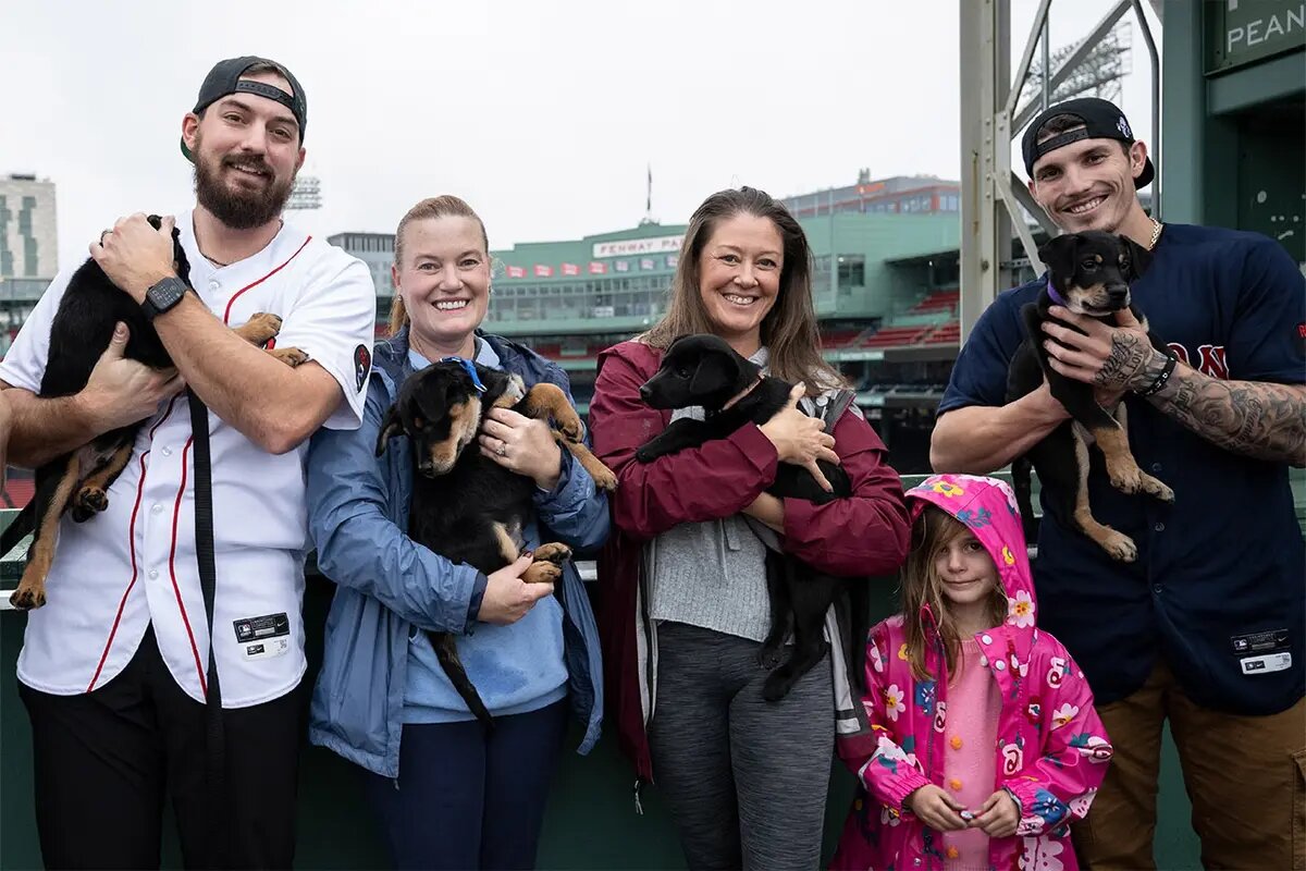 Community lifestyle photo aligned with Betsy Herald of The Charles Realty, showing a group of people holding dogs at a stadium, emphasizing relationships and personal branding